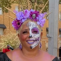 A woman smiling in elaborate sugar skull face paint with a purple flower crown at the festival