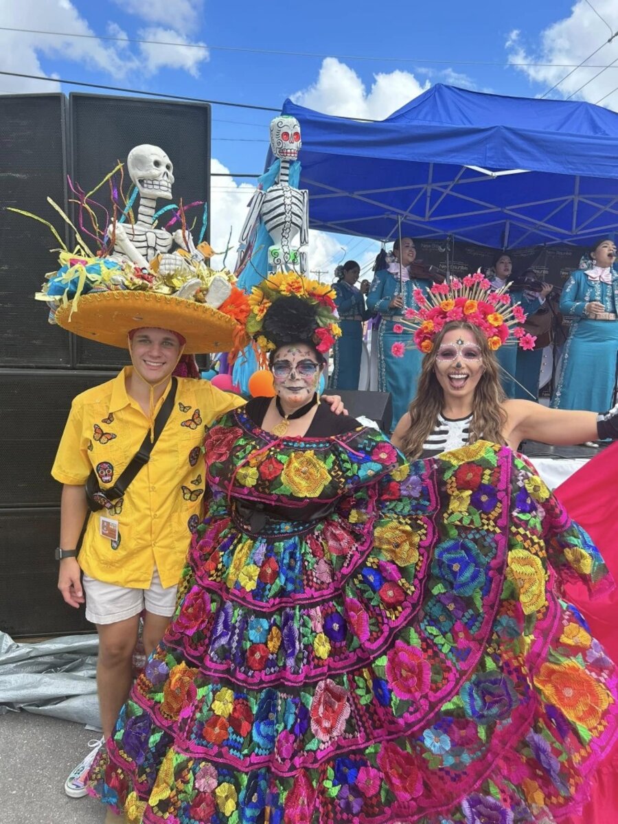 Festival-goers in flower crowns and skeleton-themed hats posing in front of the mariachi stage at night