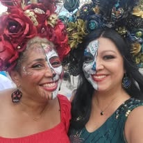 Two women with half-and-half sugar skull face paint and flower crowns smiling together